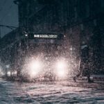 Snow-covered city street with bus during winter night snowfall, enhancing urban atmosphere.