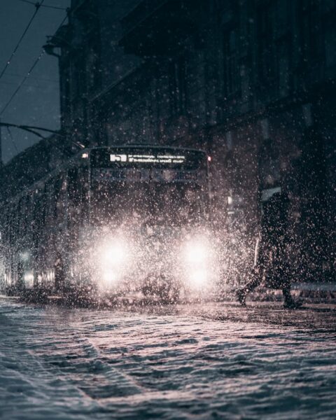 Snow-covered city street with bus during winter night snowfall, enhancing urban atmosphere.