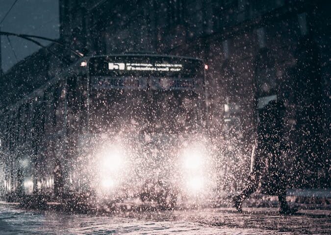 Snow-covered city street with bus during winter night snowfall, enhancing urban atmosphere.