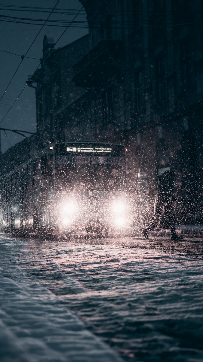 Snow-covered city street with bus during winter night snowfall, enhancing urban atmosphere.