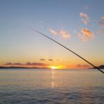 Serene sunset view with fishing silhouette over calm bay waters.
