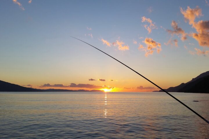 Serene sunset view with fishing silhouette over calm bay waters.