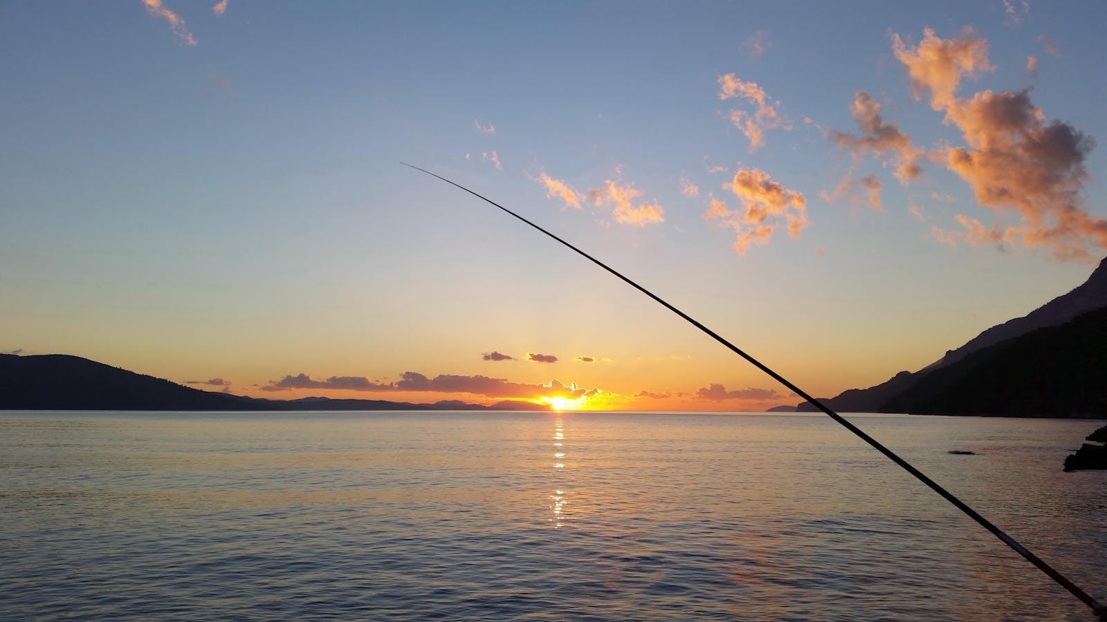 Serene sunset view with fishing silhouette over calm bay waters.