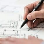 Close-up of hand drawing intricate technical designs on blueprint with pen, ideal for engineering or architecture themes.