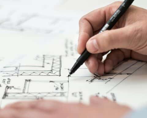 Close-up of hand drawing intricate technical designs on blueprint with pen, ideal for engineering or architecture themes.