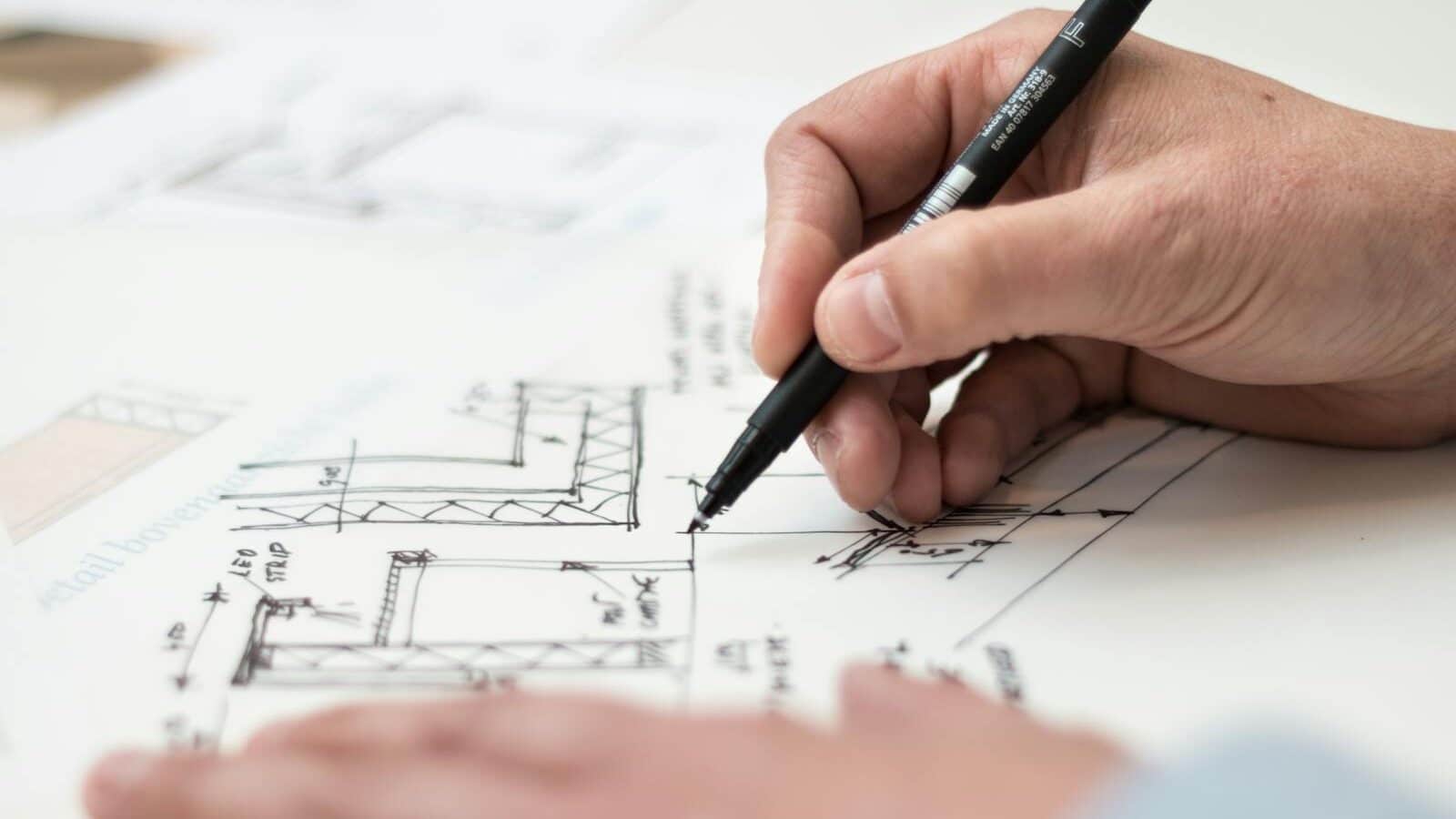 Close-up of hand drawing intricate technical designs on blueprint with pen, ideal for engineering or architecture themes.