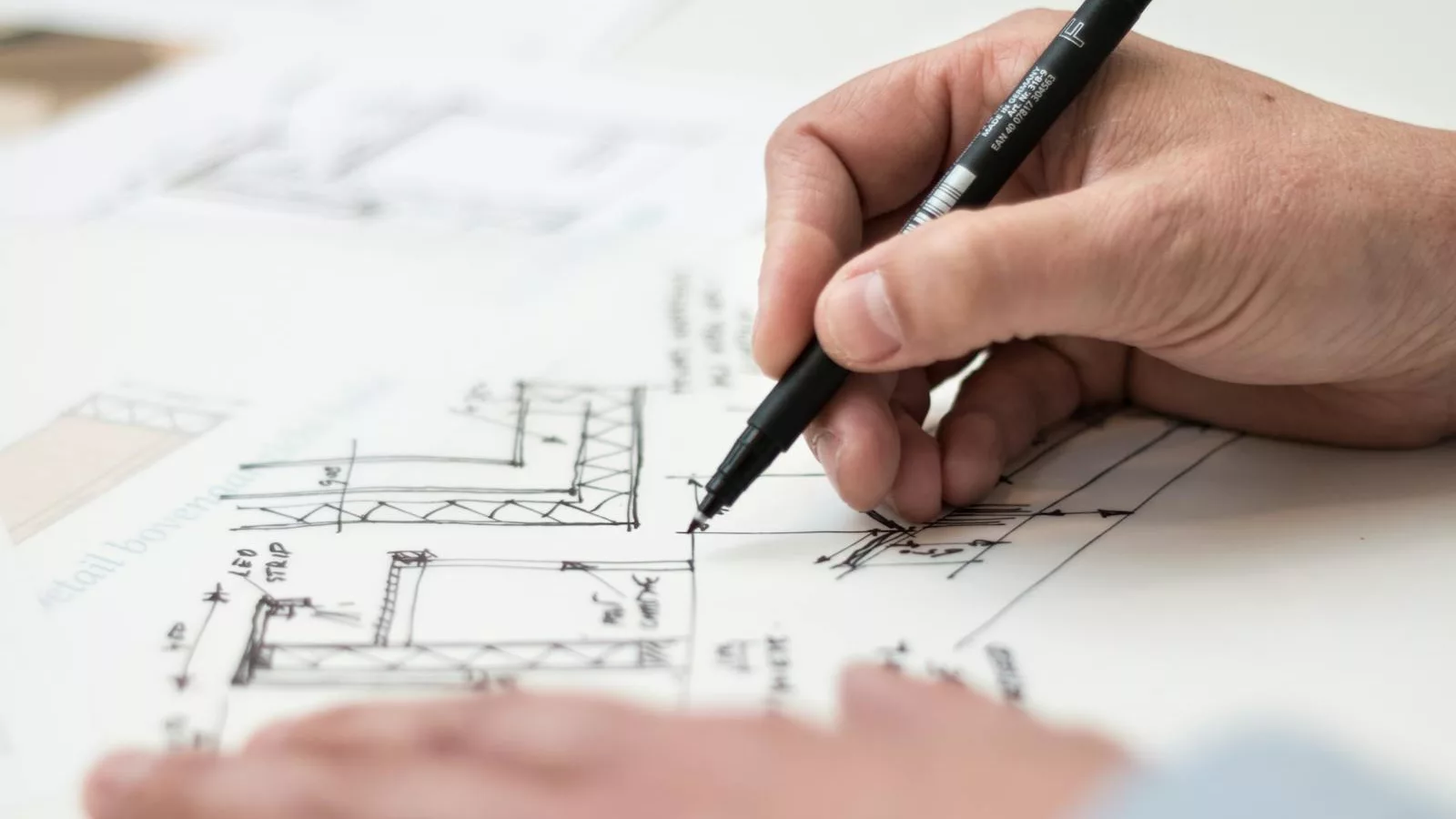 Close-up of hand drawing intricate technical designs on blueprint with pen, ideal for engineering or architecture themes.