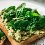 Close-up of a homemade avocado and spinach sandwich on whole grain toast.