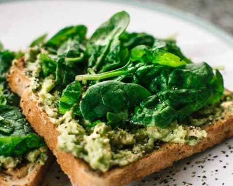 Close-up of a homemade avocado and spinach sandwich on whole grain toast.