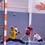 Dynamic action shot of a women's handball match with players in mid-movement.