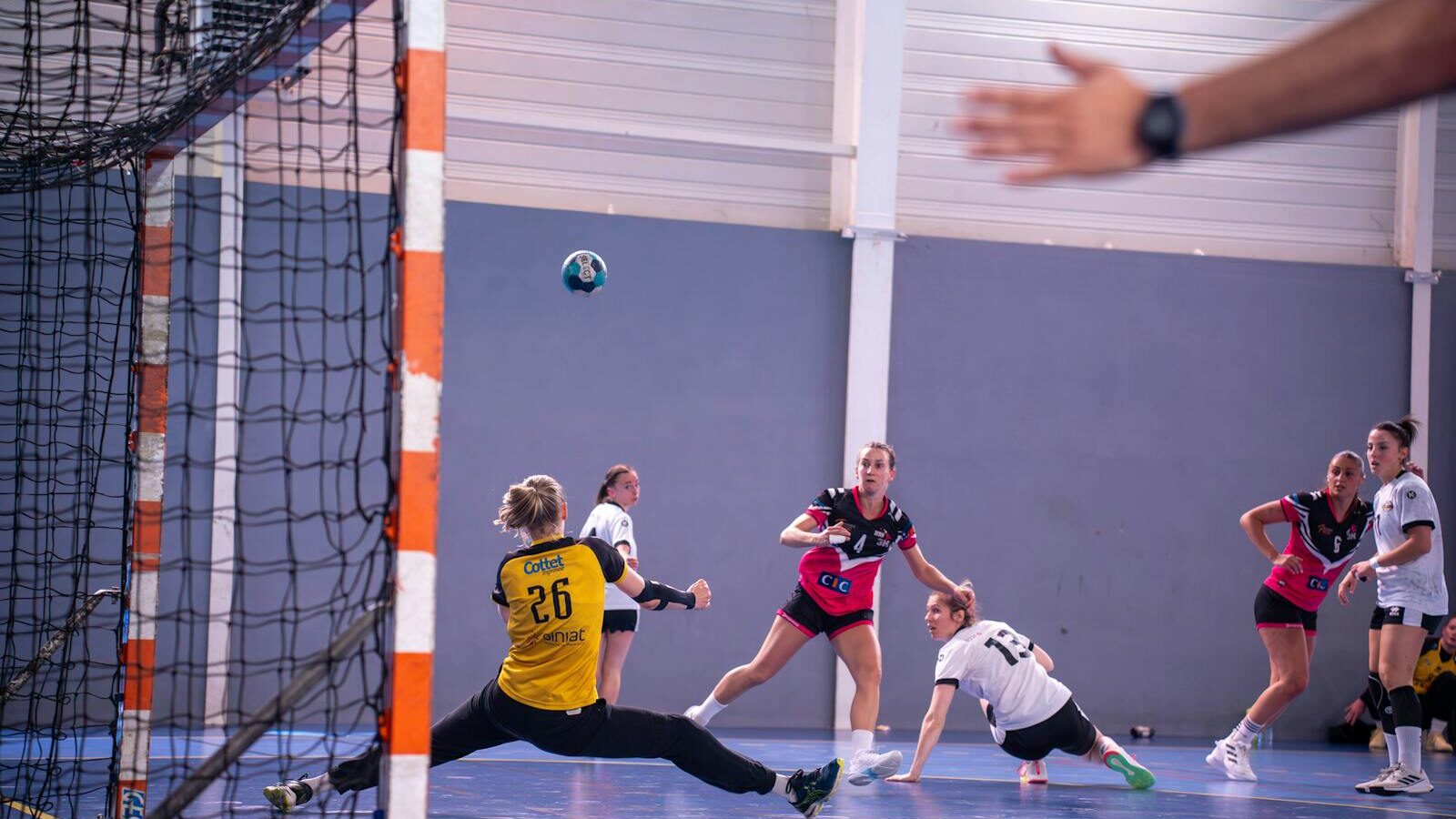 Dynamic action shot of a women's handball match with players in mid-movement.
