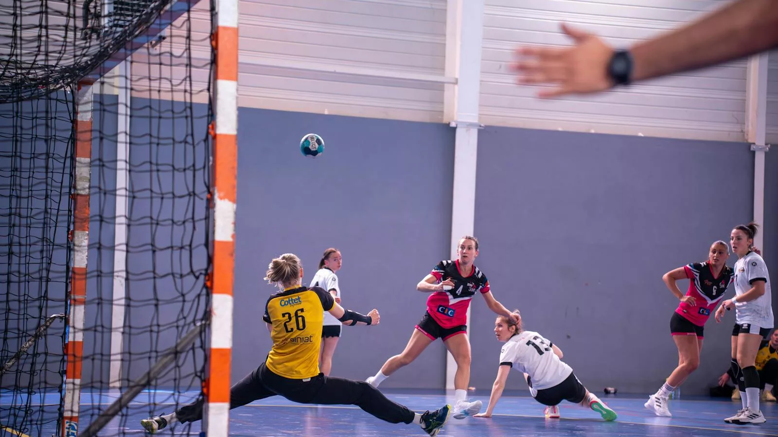 Dynamic action shot of a women's handball match with players in mid-movement.