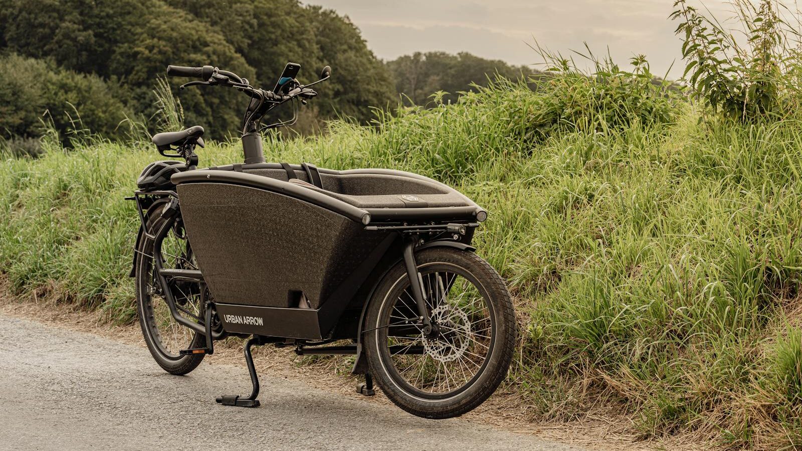 Vintage black cargo bike parked by grassy roadside in Düsseldorf, Germany.