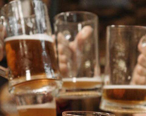 Group of friends clinking beer mugs, enjoying a fun gathering indoors.