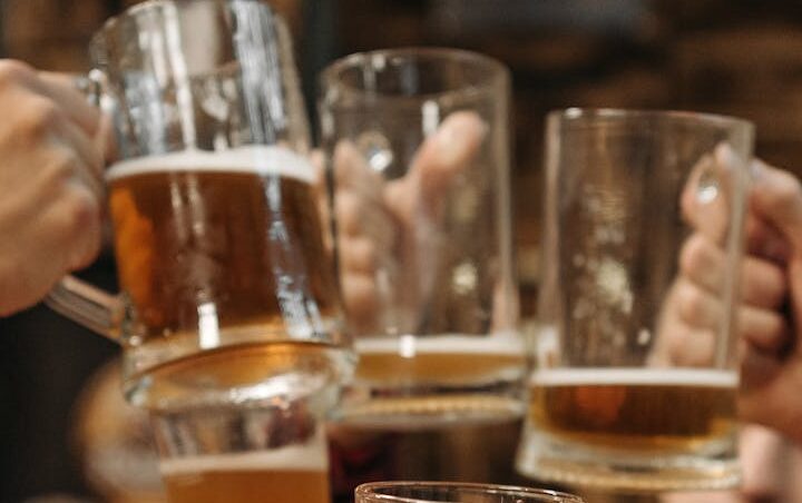 Group of friends clinking beer mugs, enjoying a fun gathering indoors.