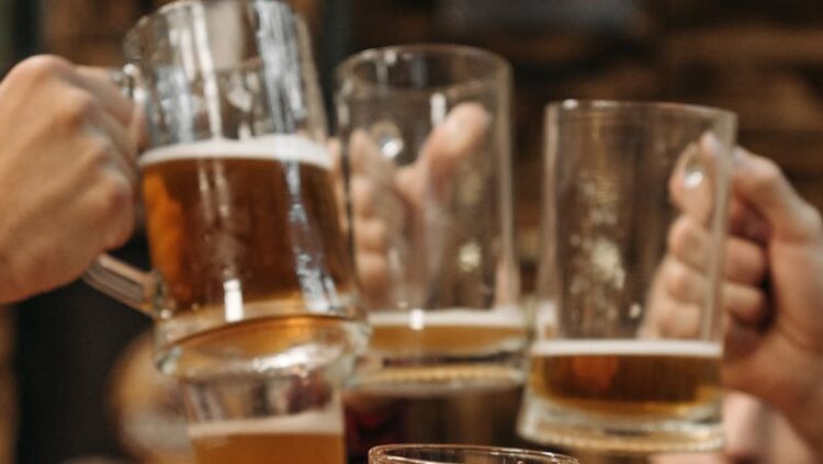 Group of friends clinking beer mugs, enjoying a fun gathering indoors.