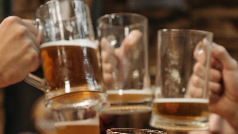 Group of friends clinking beer mugs, enjoying a fun gathering indoors.