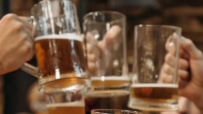 Group of friends clinking beer mugs, enjoying a fun gathering indoors.