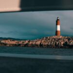 Scenic view of a lighthouse on a rocky island framed by a boat window.
