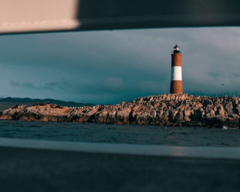 Scenic view of a lighthouse on a rocky island framed by a boat window.