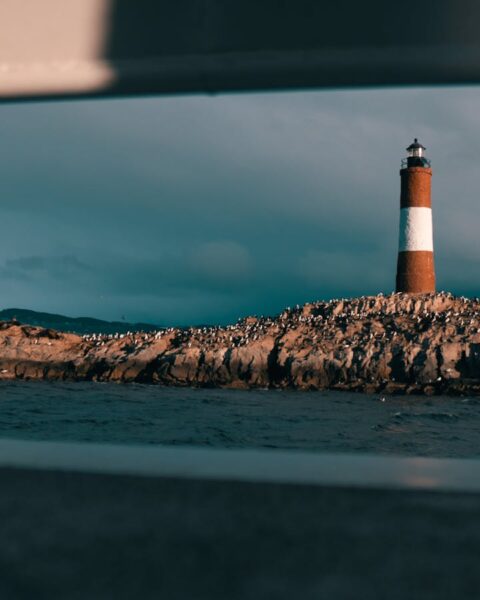 Scenic view of a lighthouse on a rocky island framed by a boat window.