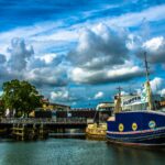 A vibrant view of Stralsund harbor featuring a sailboat, blue skies, and a bridge in the background.