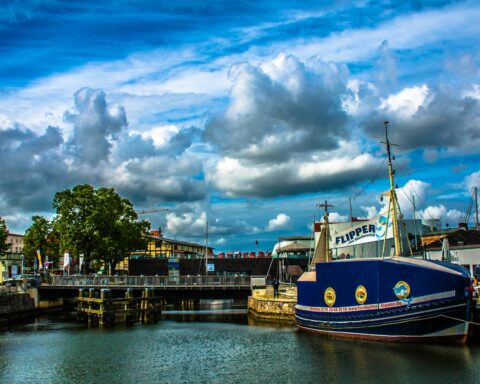 A vibrant view of Stralsund harbor featuring a sailboat, blue skies, and a bridge in the background.