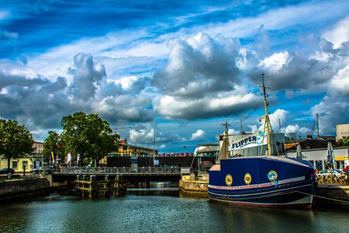 A vibrant view of Stralsund harbor featuring a sailboat, blue skies, and a bridge in the background.
