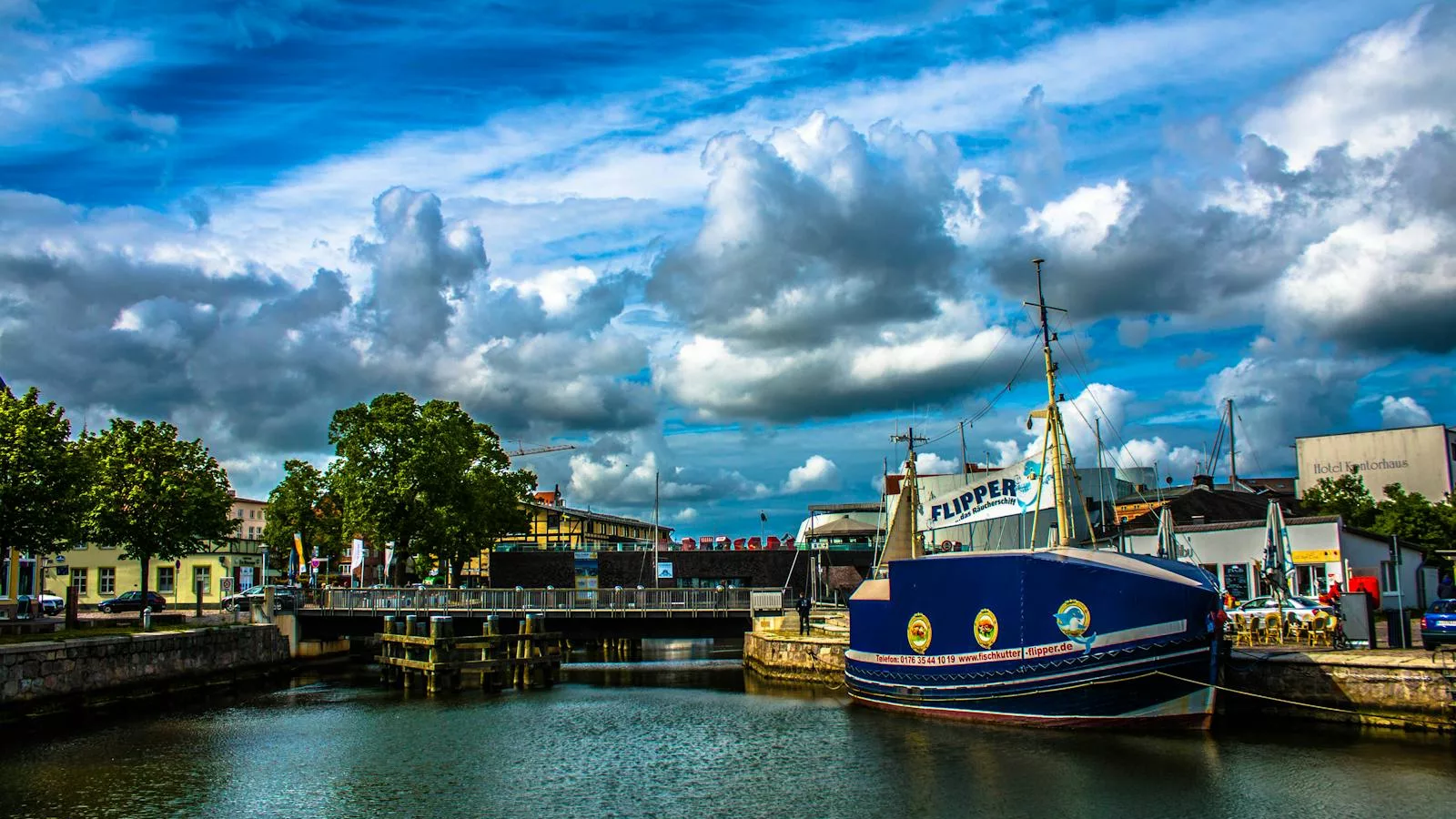 A vibrant view of Stralsund harbor featuring a sailboat, blue skies, and a bridge in the background.